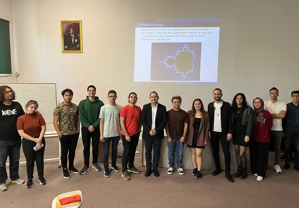Students standing in a seminar room in front of a projected slide about complex dynamics